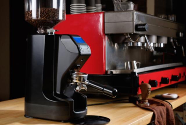 Moledora eléctrica de café, y máquina de café espresso en el fondo.    